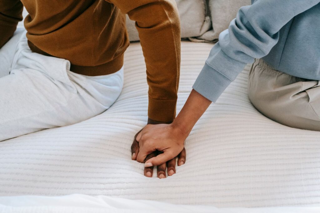 Couple holding hands on a bed, babyproofing your relationship before the baby arrives