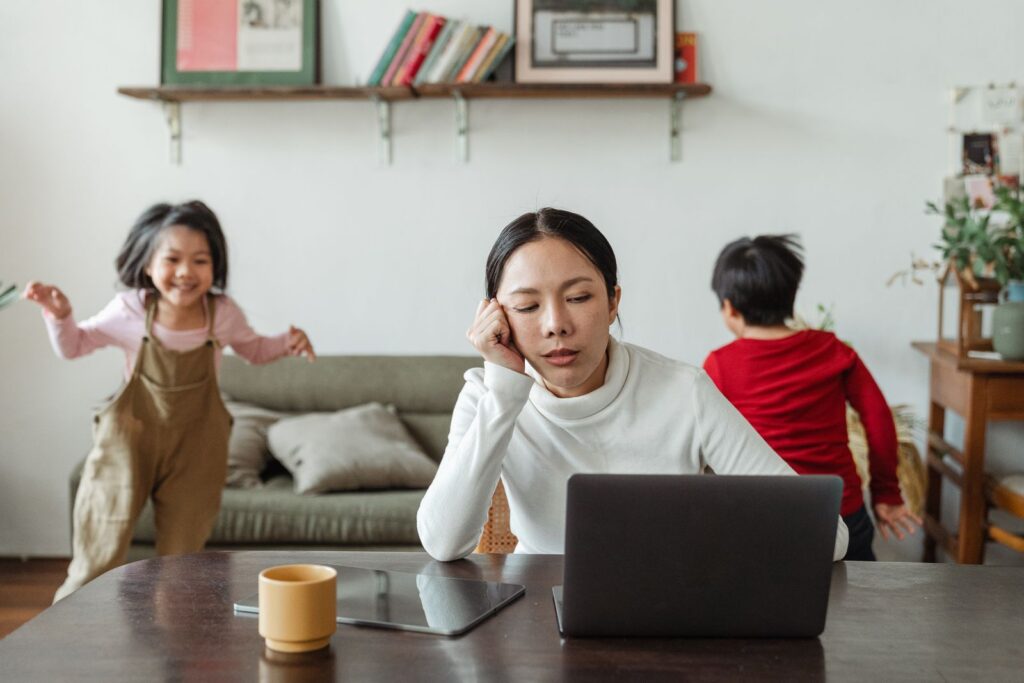 Overwhelmed mother at her laptop while her children play, wondering if it is big enough for therapy