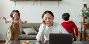 Overwhelmed mother at her laptop while her children play, wondering if it is big enough for therapy