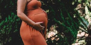 Pregnant woman in an orange dress outdoors, looking for Denver resources for pregnant and new parents
