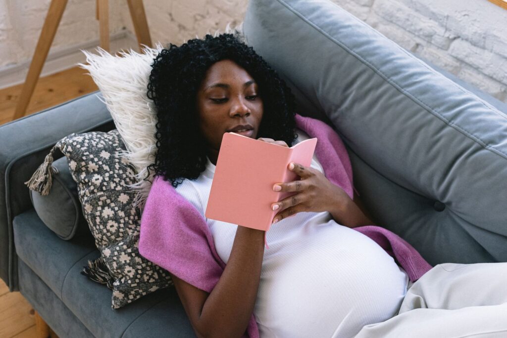 Pregnant woman resting on the couch and writing in a journal while preparing emotionally for motherhood