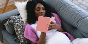 Pregnant woman resting on the couch and writing in a journal while preparing emotionally for motherhood