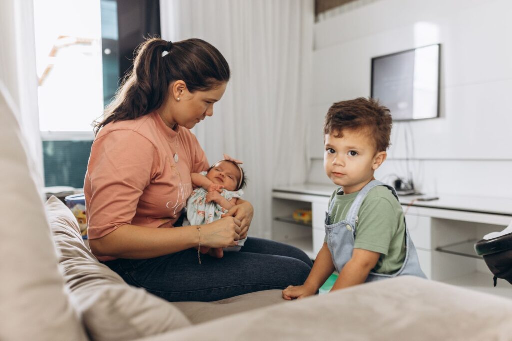 Mother holding her newborn while her toddler sits beside her during the transition from one child to two