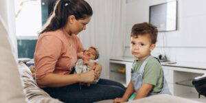 Mother holding her newborn while her toddler sits beside her during the transition from one child to two